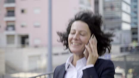 Smiling-businesswoman-talking-on-phone-while-walking-on-street